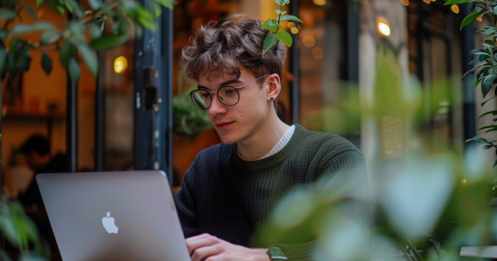 An attractive young man in his early 20s is diligently working on his laptop, managing his online business to earn money.